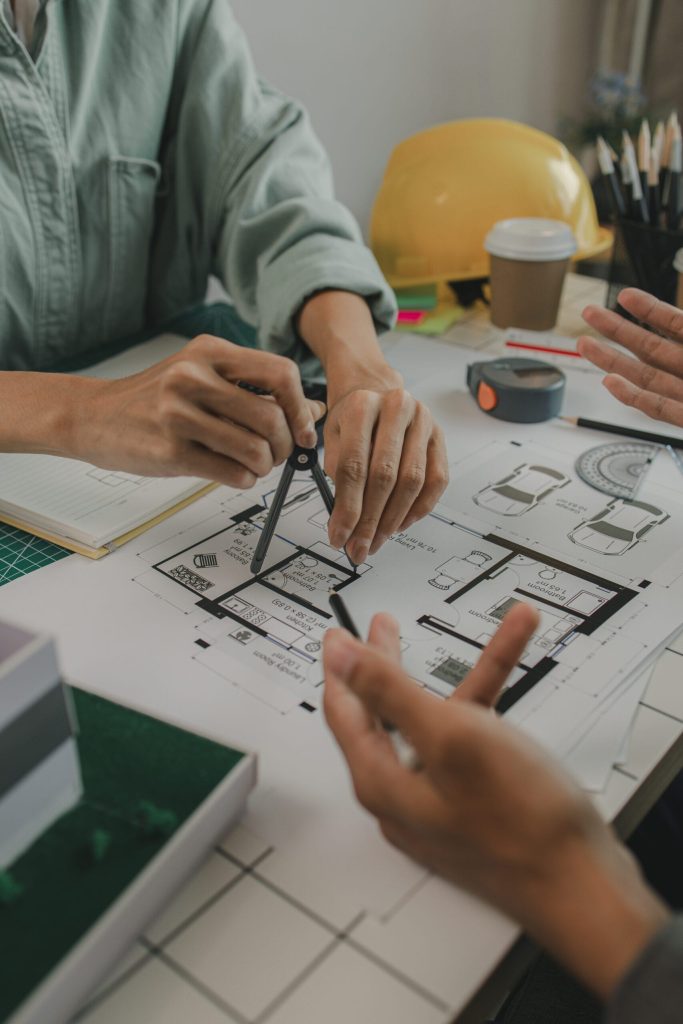 engineers are sitting discussing a construction plan that needs to be revised to make the structure stronger, an architect and assistant are brainstorming and examining the blueprints